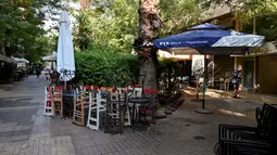 Pejalan kaki berjalan melewati restoran dan kafe yang tutup di pusat Athena, Yunani, Selasa (16/11/2021). Pemilik restoran, kafe, dan bar melakukan pemogokan selama 24 jam, memprotes aturan terkait Covid-19 dan biaya energi yang tinggi. (Louisa GOULIAMAKI / AFP)