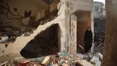 Seorang wanita Palestina berdiri di samping puing-puing di luar gedung yang menjadi sasaran serangan udara Israel pada 12 Desember 2024 di dekat pengungsi Nuseirat di Jalur Gaza tengah. (Eyad BABA/AFP)