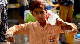Seorang anak laki-laki bereaksi setelah mengisi botol dengan air dari truk tangki air di lingkungan berpenghasilan rendah di New Delhi pada Kamis (3/6/2021). Kelangkaan air secara tidak proporsional mempengaruhi orang-orang rentan di masyarakat berpenghasilan rendah. (Money SHARMA / AFP)