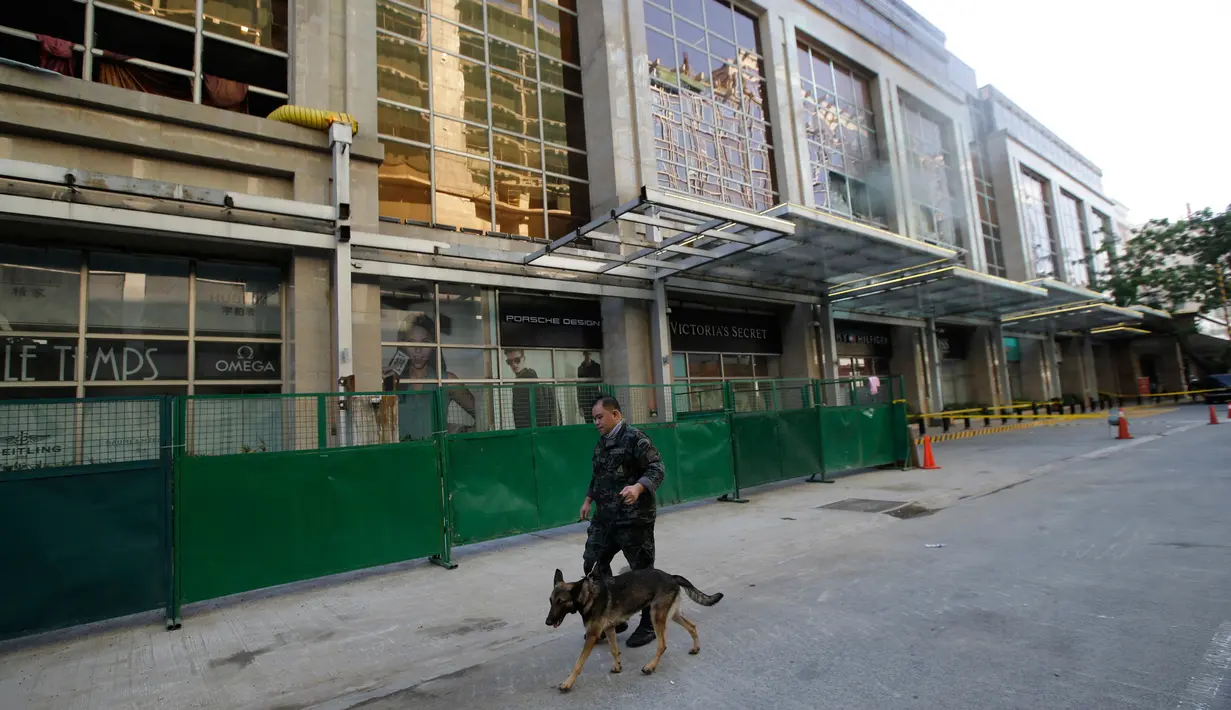 Petugas bersama anjing pelacak melewati area hotel yang berasap di kompleks Resorts World Manila, Jumat (2/6). Serangan pria bersenjata dilaporkan telah melukai puluhan tamu hotel dan kasino yang berlarian setelah penembakan muncul (AP Photo/Aaron Favila)
