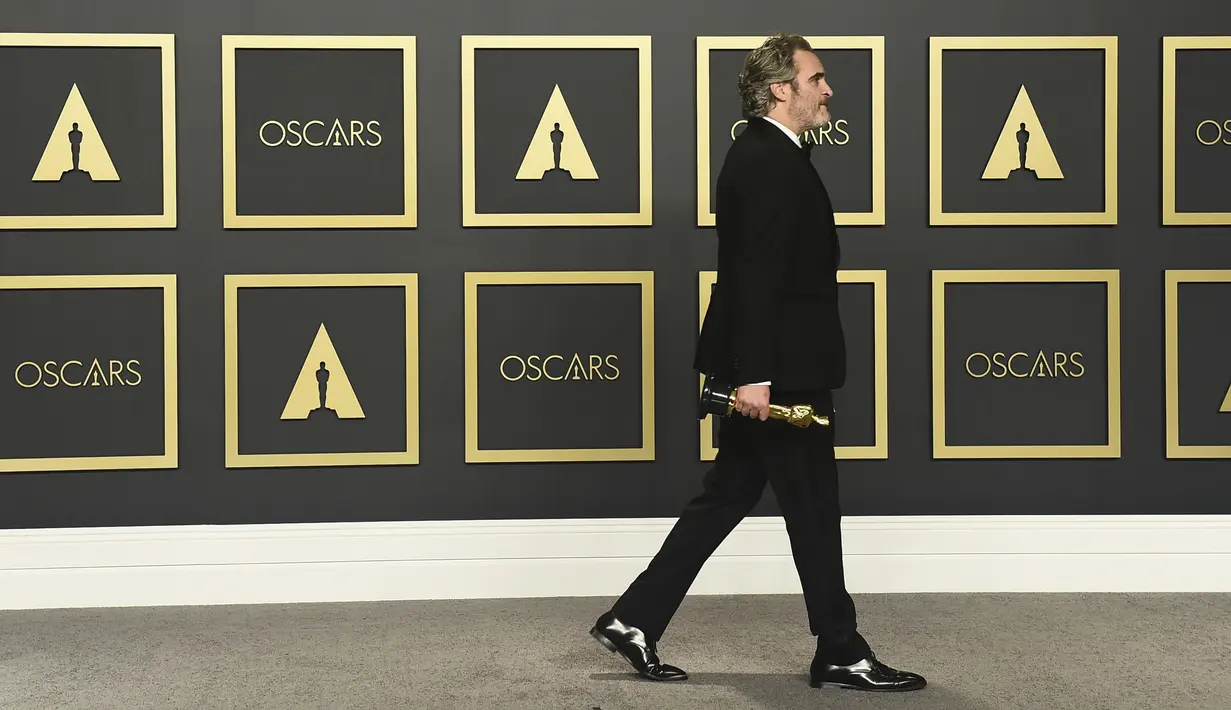 Aktor Joaquin Phoenix berjalan membawa piala Oscar 2020 usai berpose di ruang pers di  Dolby Teater, Los Angeles, Minggu (9/2/2020). Joaquin Phoenix yang memerankan karakter Arthur Fleck dalam film Joker, meraih penghargaan Oscar 2020 untuk kategori aktor terbaik. (AP Photo/Jordan Strauss)