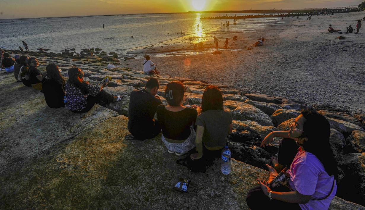Pantai Kelan menawarkan pemandangan senja yang dramatis. Saat matahari perlahan tenggelam, langit berubah oranye keemasan dan berpadu dengan siluet pesawat yang tengah lepas landas atau mendarat. Kombinasi inilah yang menciptakan pengalaman visual unik dan jarang ditemukan di pantai lain. Tampak dalam foto, aktivitas wisatawan menikmati waktu senja di Pantai Kelan, Badung, Bali. (merdeka.com/Arie Basuki)