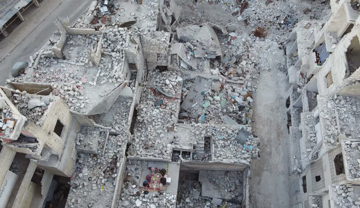 Keluarga Tareq Abu Ziad menunggu waktu berbuka puasa di tengah reruntuhan rumah mereka yang hancur setelah serangan militer pasukan pemerintah dan sekutunya di Kota Ariha, Provinsi Idlib, Suriah, Senin (4/5/2020). Muslim Suriah melewati Ramadan tahun ini masih dalam kondisi perang. (AAREF WATAD/AFP)