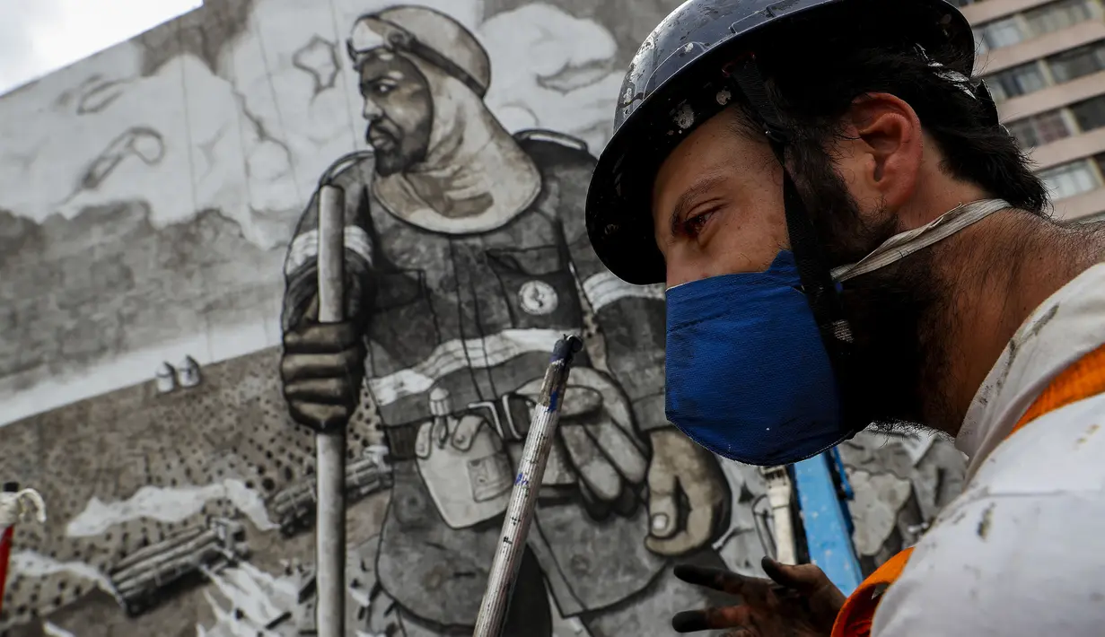 Seniman Thiago Mundano berpose di samping muralnya "The Forest Brigadir" dari abu kebakaran hutan Amazon yang menutupi kompleks apartemen di Sao Paulo, Jumat (15/10/2021). Mural bergambar petugas damkar yang berdiri di tengah peristiwa deforestasi, kebakaran, dan hewan mati. (AP/Marcelo Chello)