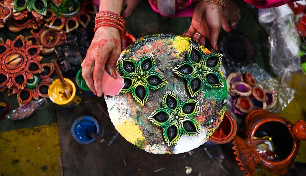 Seorang pembuat tembikar menuangkan lilin ke lampu tanah jelang Festival Diwali di sepanjang pinggir jalan di New Delhi, India, 18 Oktober 2022. Festival Diwali atau dalam agama Hindu berarti Festival Cahaya melambangkan kemenangan baik atas keburukan, dan lampu atau pelita dinyalakan sebagai tanda perayaan serta harapan umat manusia. (Sajjad HUSSAIN/AFP)