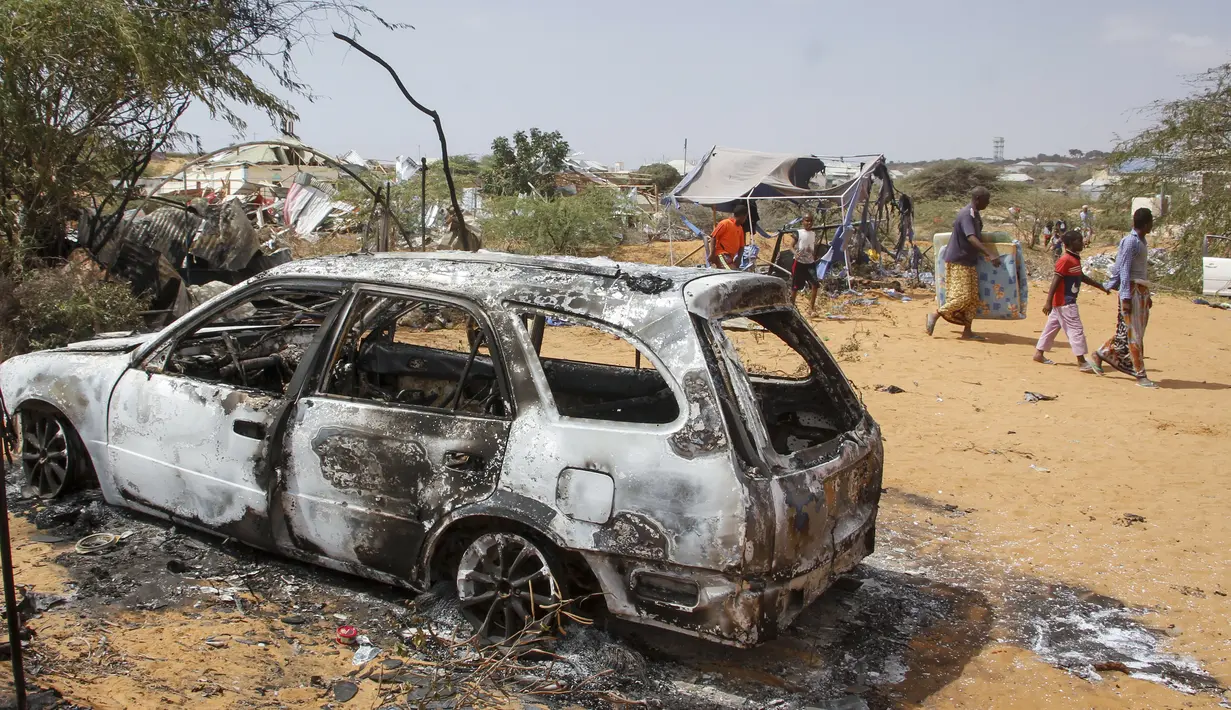 Warga berjalan melewati puing-puing kendaraan yang hancur dalam serangan terhadap polisi dan pos pemeriksaan di pinggiran ibu kota Mogadishu, Somalia (16/2/2022). Serangan oleh kelompok ekstremis al-Shabab pada hari Rabu menewaskan lima orang dan melukai 16 orang. (AP Photo/Farah Abdi Warsameh)