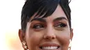 <p>Georgina Rodriguez tersenyum sambil berpose untuk fotografer setibanya di pemutaran perdana film 'Tar' selama Venice Film Festival ke-79 di Venesia, Italia (1/9/2022). Georgina memakai palet riasan perunggu sempurna dengan lipstik natural di bibirnya. (AFP/Tiziana Fabi)</p>