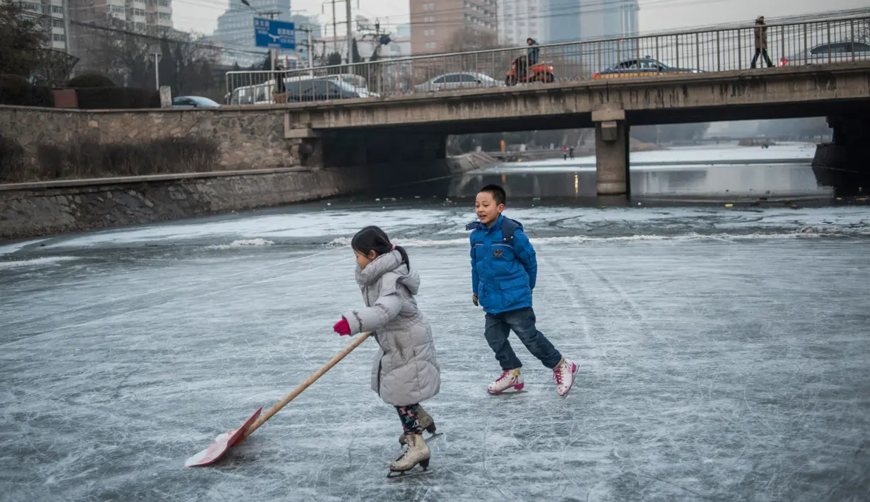 Dua orang anak asyik bermain ice skating atau seluncur es di atas sungai yang telah membeku di Beijing, Jumat (1/1). Semenjak membeku, sungai di Beijing ini menjadi objek wisata es dadakan yang banyak diminati wisatawan.  (AFP/Fred Dufour)