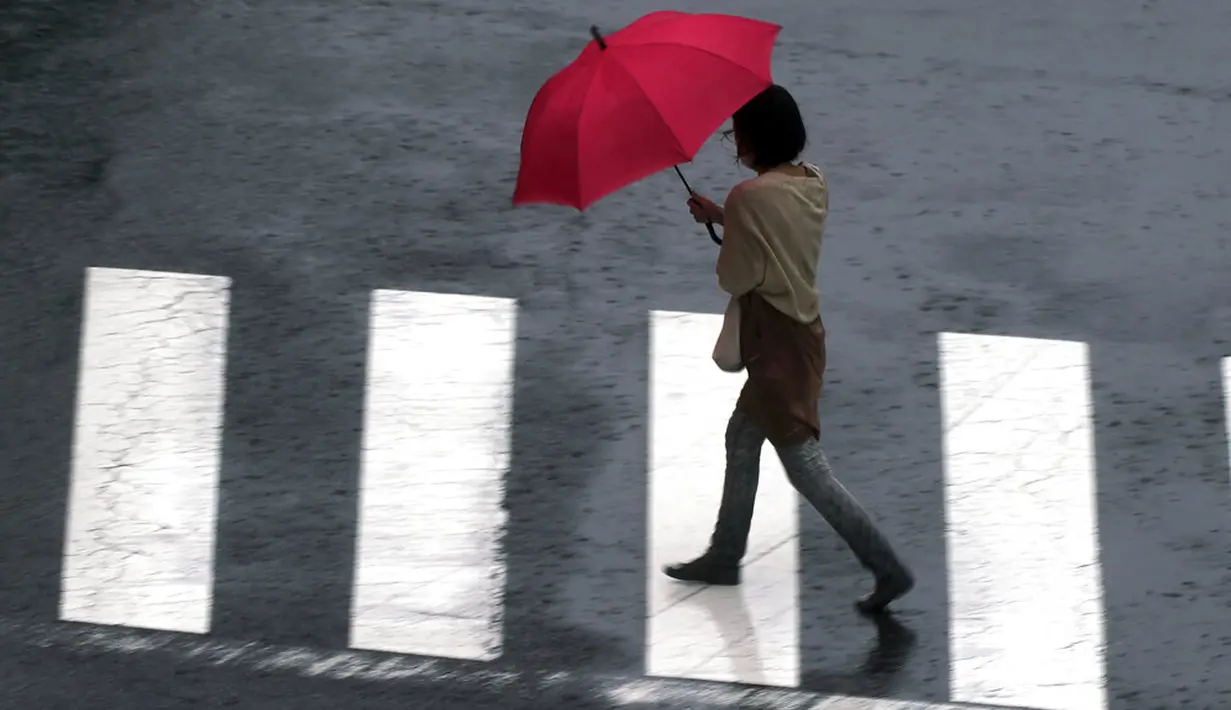 Seorang wanita menyeberang jalan di tengah hujan dari Topan Mindulle di Tokyo, Jepang, Jumat (1/10/2021). Topan Mindulle sedang bergerak di lepas pantai Jepang. (AP Photo/Eugene Hoshiko)