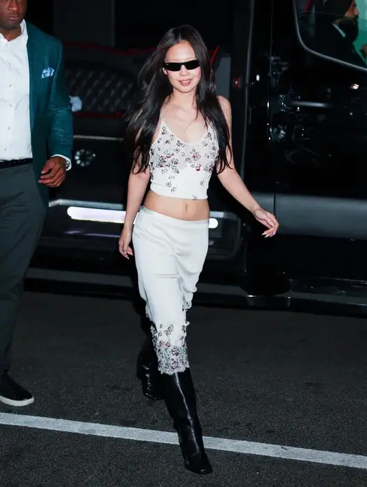 Masih setia dengan rumah mode Chanel, Jennie memilih tampilan yang lebih effortless namun tetap statement. Ia mengenakan cropped lace camisole dengan detail sequin halus yang dipadukan dengan satin midi skirt senada, memperlihatkan siluet midriff yang sleek. Sentuhan edgy hadir lewat knee-high leather boots serta sunglasses, memberi kontras modern pada look yang feminin. [@voguehongkong].