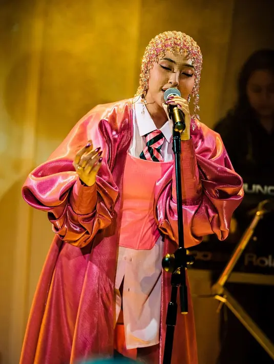Tampilan nyentrik Jinan diciptakan dengan outfit layering. Ia padukan kemeja, korset, dan outer pink saat manggung. Lengkap dengan dasi pink hitam yang jadi aksen maskulin. Hijab yang ia kenakan pun dilengkapi dengan headpiece jaring-jaring. [@jinanlaetitia]