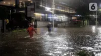 Warga melintasi banjir di Jalan Kemang Raya, Jakarta Selatan, Selasa (4/10/2022). Hujan yang mengguyur wilayah Ibu Kota Jakarta mengakibatkan banjir menggenangi kawasan Kemang, Jakarta. (Liputan6.com/Johan Tallo)