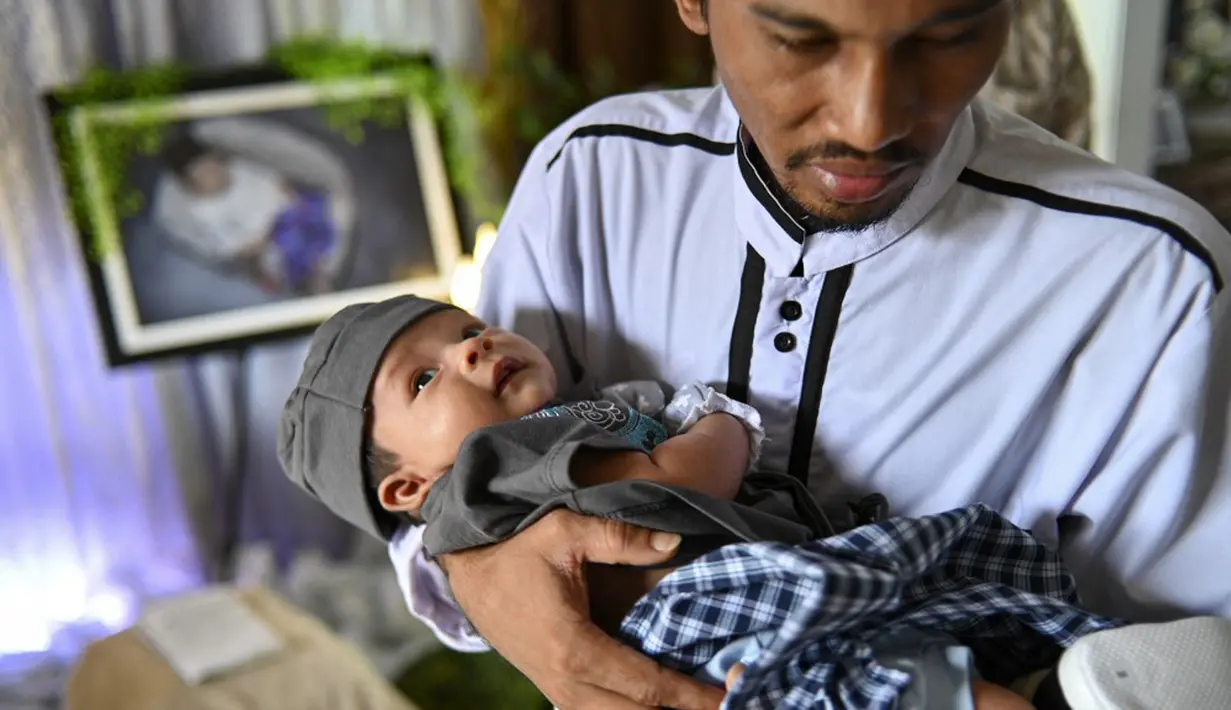 Seorang pria menggendong bayi yang baru lahir saat prosesi aqiqah di Banda Aceh, Aceh, 4 November 2021. Aqiqah adalah tradisi menyambut bayi yang baru lahir dalam agama Islam. (CHAIDEER MAHYUDDIN/AFP)