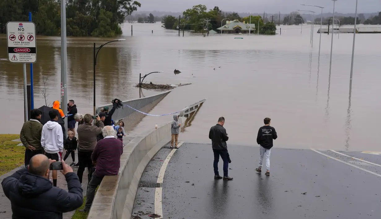 <p>Orang-orang memandangi Jembatan Windsor yang banjir di Windsor di pinggiran Sydney, Australia, Selasa (5/6/2022). Ratusan rumah terendam di dalam dan sekitar kota terbesar Australia itu dalam keadaan darurat banjir yang berdampak pada 50.000 orang, kata para pejabat. (AP Photo/Mark Baker)</p>