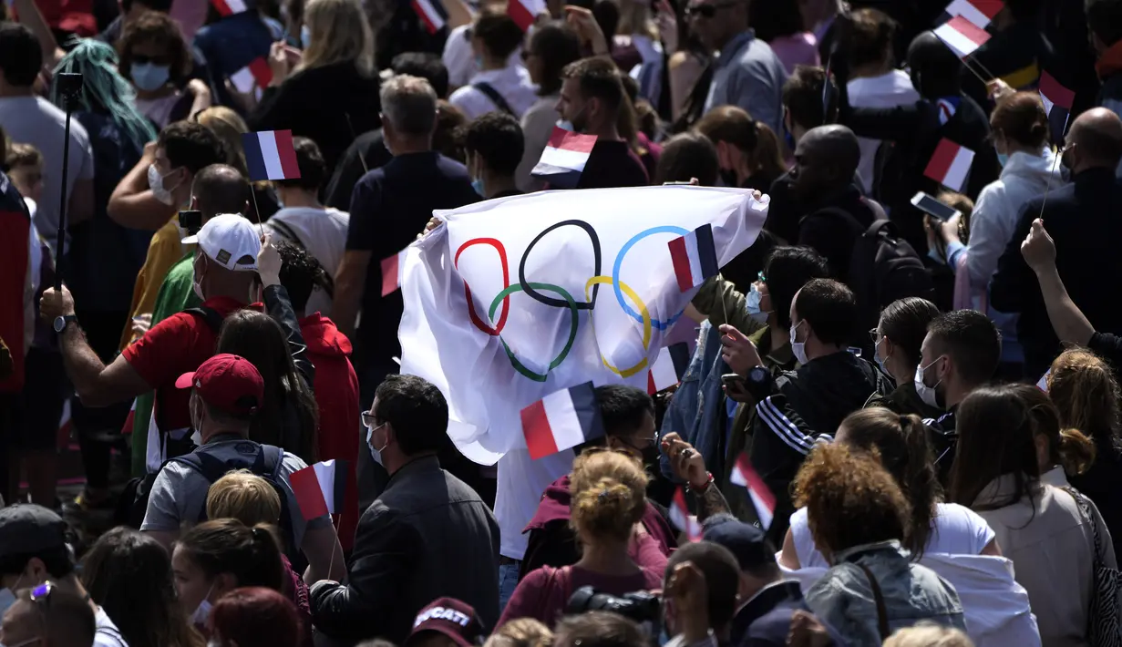 Fans membawa bendera di zona penggemar Olimpiade di Trocadero Gardens di depan Menara Eiffel di Paris, Minggu (8/8/2021). Pelepasan tongkat tuan rumah akan dibagi antara Stadion Olimpiade di Tokyo dan pesta publik dan konser di Paris. (AP Photo/Francois Mori)