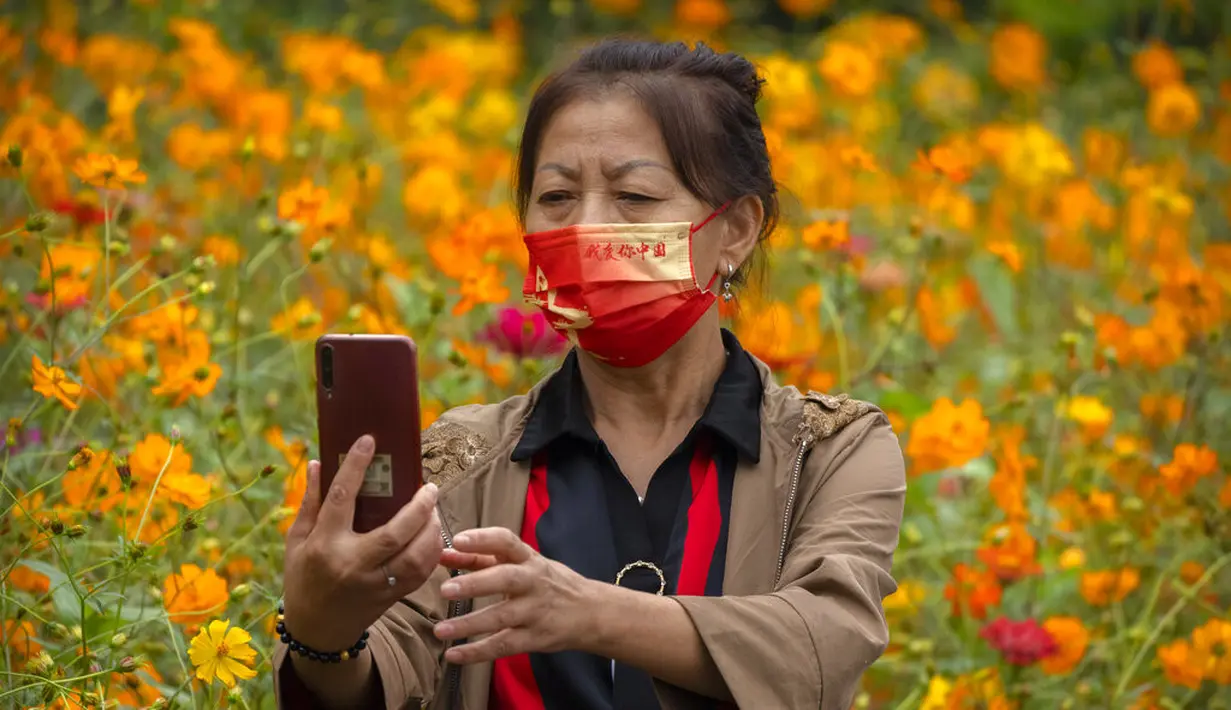 Seorang wanita mengenakan masker bertuliskan "I love you China" berpose untuk selfie dengan bunga mekar di taman umum di Beijing, Sabtu (2/10/2021). Pengunjung memadati taman dan lokasi wisata di Beijing saat China merayakan hari kedua masa libur Hari Nasional. (AP Photo/Mark Schiefelbein)