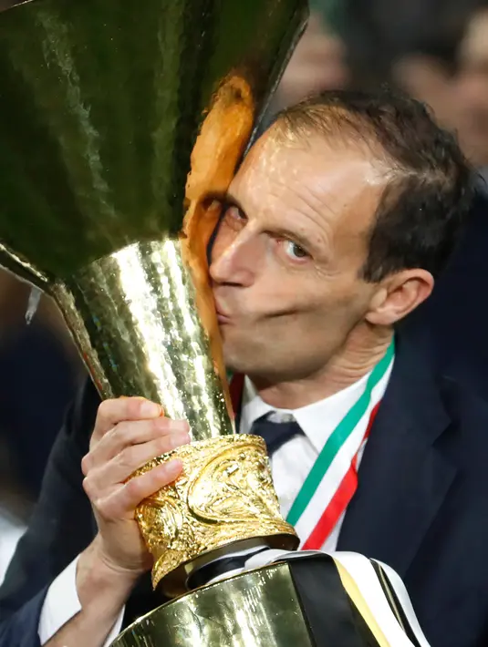 Pelatih Juventus, Massimiliano Allegri mencium Piala Liga Italia Serie A usai menjuarainya untuk ke-33 kalinya di Stadion Allianz, Turin (19/5/2019). Juventus meraih gelar scudetto kedelapan secara beruntun sekaligus rekor baru. (AP Photo/Antonio Calanni)