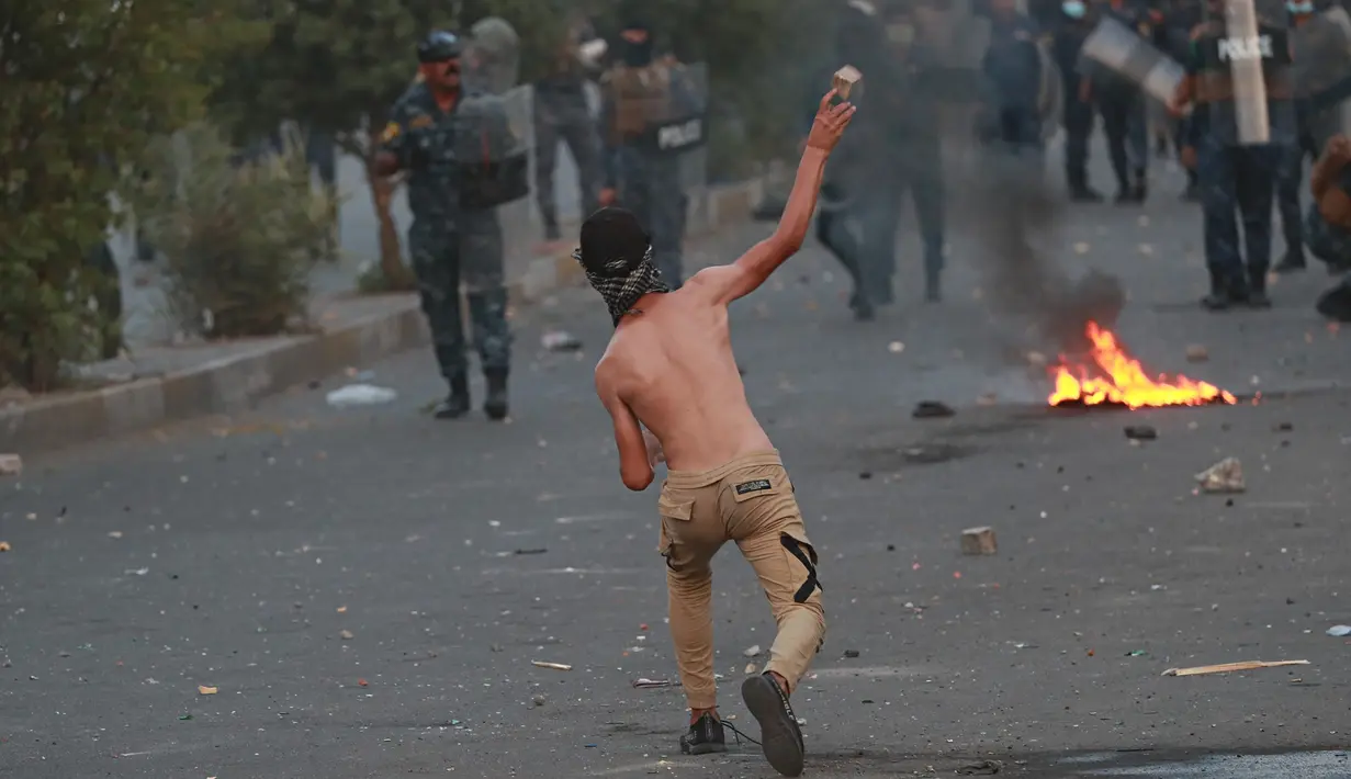 Seorang demonstran antipemerintah melemparkan batu ke arah pasukan keamanan saat protes di dekat Alun-Alun Tahrir, Baghdad, Irak, Senin (27/7/2020). Perdana Menteri Irak mengatakan telah memerintahkan penyelidikan atas pembunuhan dua demonstran antipemerintah. (AP Photo/Hadi Mizban)
