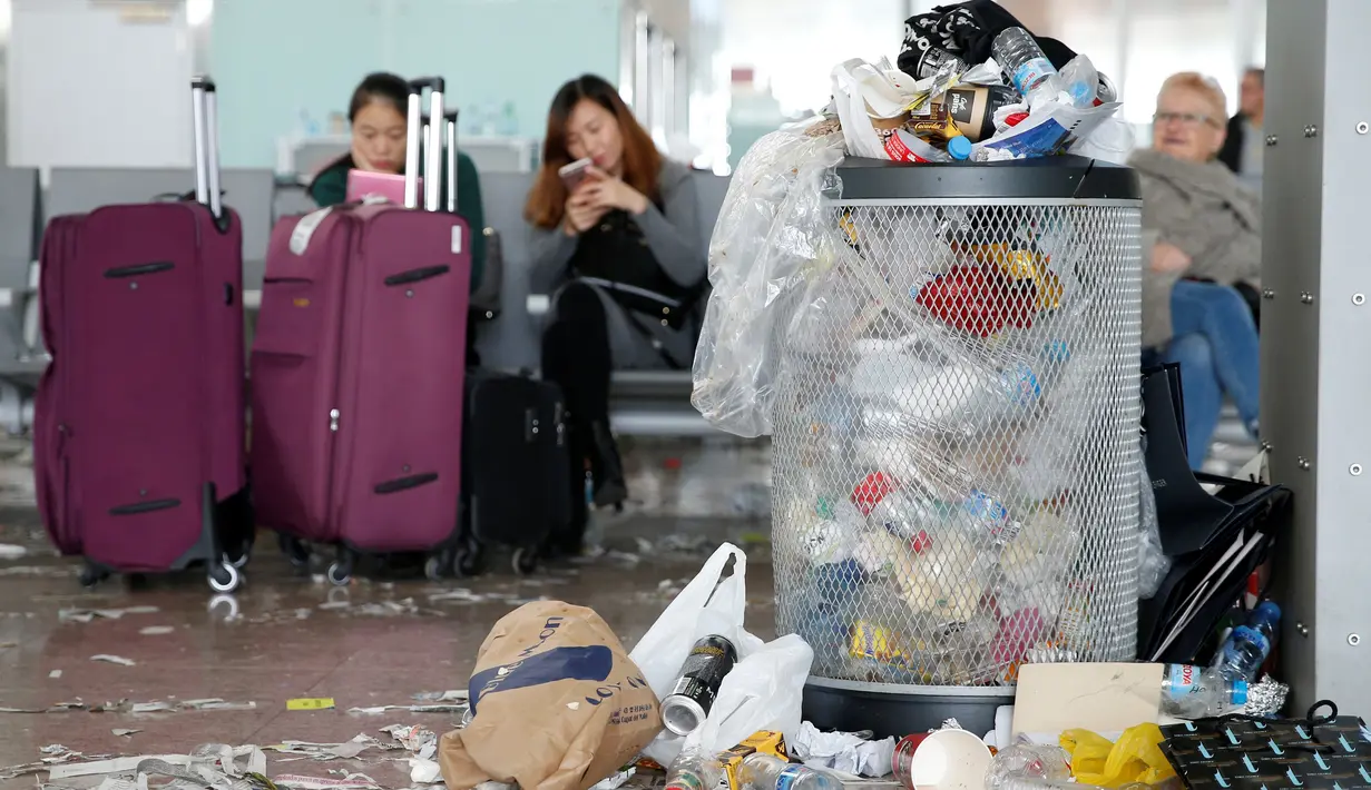 Tumpukan sampah terlihat di dekat penumpang yang menunggu jadwal penerbangan di Bandara Barcelona, Spanyol, Kamis (1/12). Para petugas kebersihan melakukan aksi protes mengotori ruangan bandara dengan sampah sobekan kertas. (REUTERS/Albert Gea)
