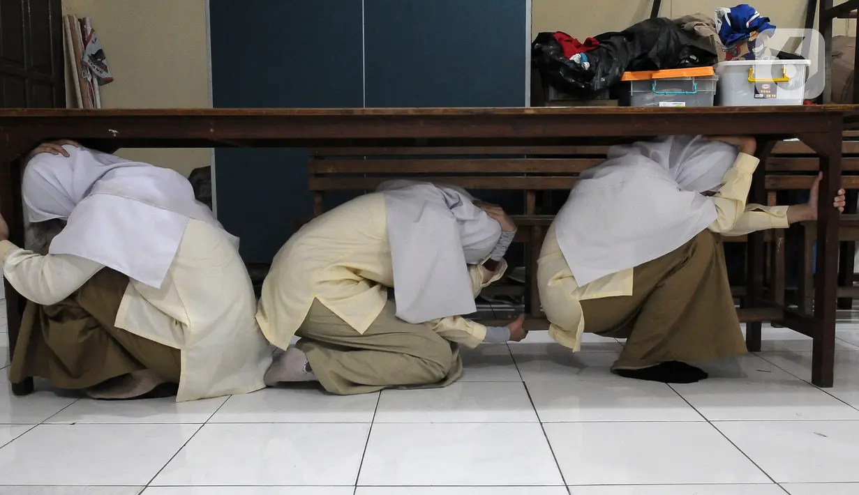 Sejumlah santriwati berlindung di bawah meja saat pelatihan tanggap bencana dan kebakaran yang dilakukan oleh Badan Penanggulangan Bencana Daerah (BPBD) DKI Jakarta bersama Pemadam Kebakaran DKI Jakarta di Madrasah Aliyah Swasta Persatuan Islam (MAS Persis) 69, Matraman, Jakarta, Selasa (19/9/2023). (merdeka.com/Imam Buhori)