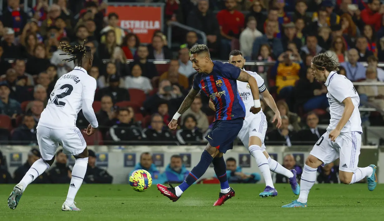 Pemain Barcelona, Raphinha (tengah) berusaha melewati pemain Real Madrid pada laga pekan ke-26 Liga Spanyol 2022/2023 di Camp Nou, Barcelona, Senin (20/03/2023). Blaugrana menang dengan skor 2-1 pada pertandingan yang bertajuk El Classico tersebut. (AP Photo/Joan Monfort)