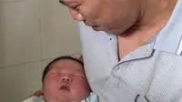 Tran Van Quan menggendong bayi laki-lakinya, Tran Tien Quoc di pusat kesehatan Vinh Tuong, provinsi Vinh Phuc, Vietnam, Minggu (15/10). Bayi laki-laki tersebut lahir melalui operasi Caesar pada 14 Oktober 2017 lalu. (LE PHUONG/AFP)