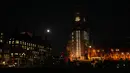 Bulan purnama pertama tahun ini atau Wolf Moon terlihat di belakang London Eye dan tampilan jam saat perbaikan Menara Elizabeth, yang dikenal sebagai Big Ben dan Gedung Parlemen, di London, Senin (17/1/2022). Wolf Moon adalah sebutan untuk bulan purnama pertama di Januari. (AP Photo/Matt Dunham)