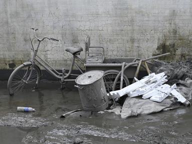 Sebuah sepeda roda tiga yang tertutup lumpur terlihat di dekat rumah seorang warga setelah banjir akibat hujan lebat di kota Zhuozhou, di provinsi Hebei, China utara, Rabu (9/8/2023). (Jade Gao / AFP)