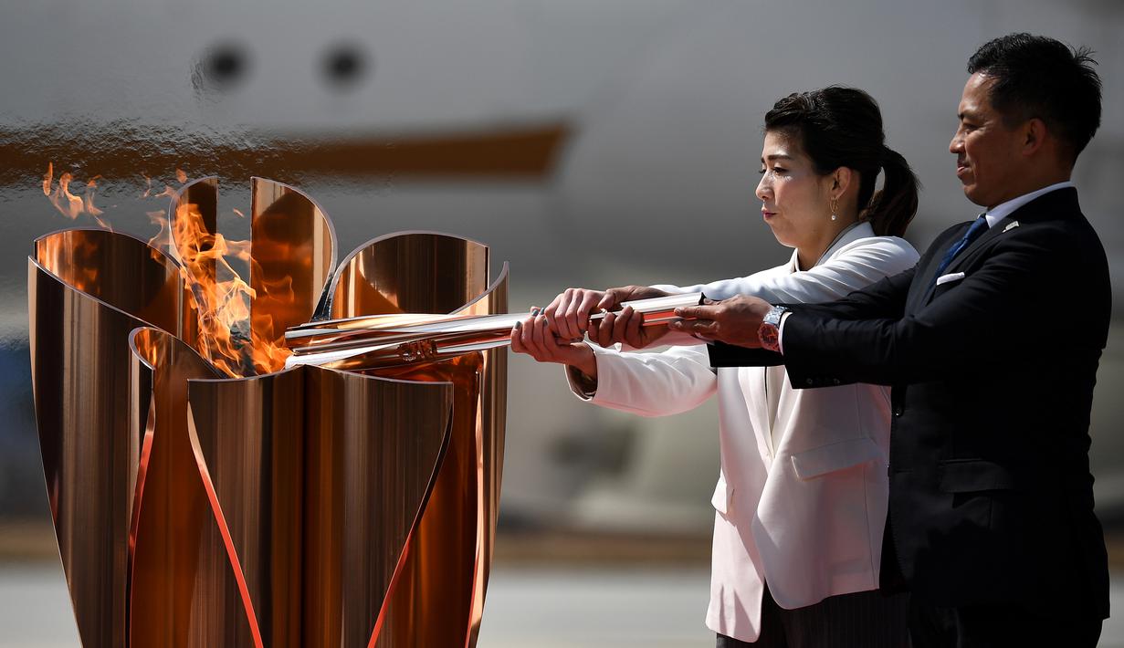 Atlet peraih tiga kali medali emas olimpiade, Tadahiro Nomura dan Saori Yoshida, menyalakan obor Olimpiade saat tiba dari Yunani di Pangkalan Udara Matsushima, Jepang, Jumat (20/3). Prosesi menuju Olimpiade Tokyo 2020 masih terus berjalan.(AFP/Philip Fong)