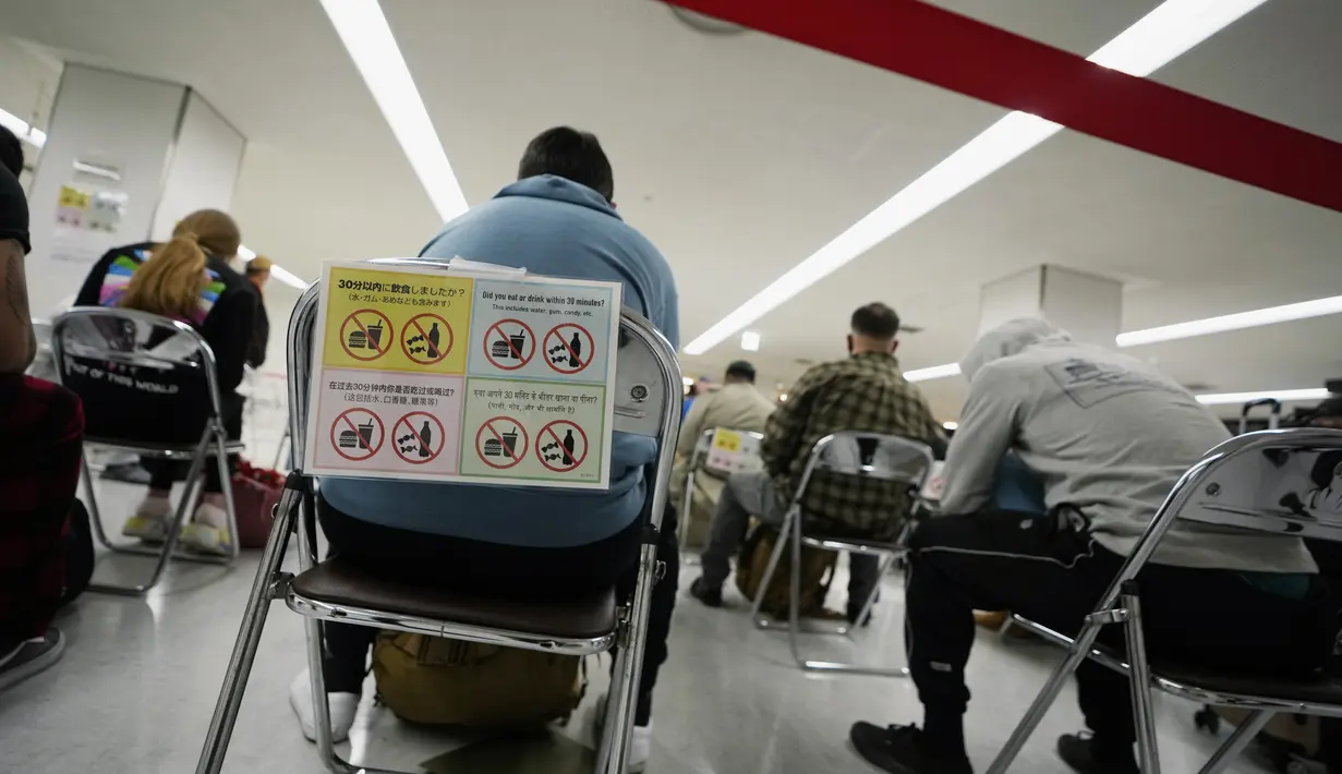 Penumpang duduk dan menunggu giliran selama proses karantina pencegahan virus corona setelah mendarat di Bandara Internasional Narita di Narita, timur Tokyo, Jepang (2/12/2021). Kasus pertama varian baru Covid-19 Omicron terdeteksi di Bandara Narita, Jepang.  (AP Photo/Hiro Komae)