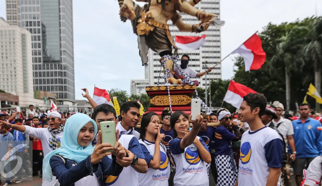 Simpatisan Partai NasDem berselfie saat pawai ogoh-ogoh dalam aksi Kita Indonesia di kawasan Bundaran HI, Jakarta, Minggu (04/12). Aksi tersebut diisi dengan parade budaya Indonesia dan orasi tokoh politik nasoional Indonesia. (Liputan6.com/Fery Pradolo)