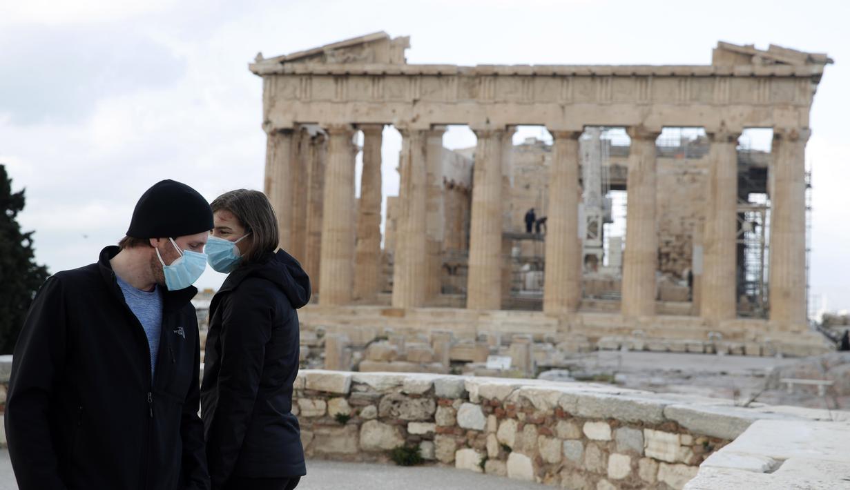 Pengunjung pertama yang mengenakan masker wajah berdiri di atas bukit Acropolis, dengan latar belakang kuil Parthenon di Athena, Senin (22/3/2021). Pemerintah Yunani membuka kembali Acropolis dan situs kuno lainnya secara nasional untuk memulai kembali musim pariwisata pada pertengahan Mei. (AP Phot