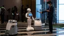 Seorang reporter (kanan) merekam suara salam dari robot Pepper (tengah) dan dua robot pembersih di hotel yang diubah menjadi lokasi karantina pasien COVID-19, Tokyo, Jepang, Jumat (1/5/2020). Sejumlah hotel menyediakan layanan robot ini untuk meringankan beban rumah sakit. (Philip FONG/AFP)