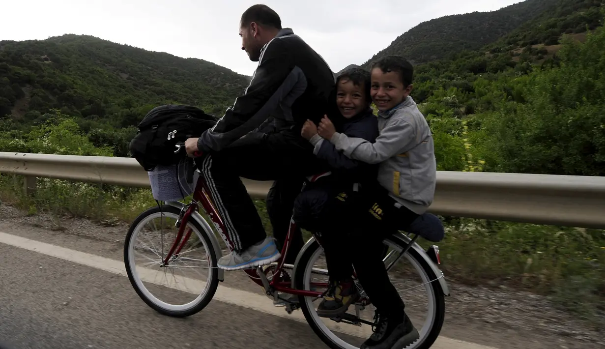 Seorang imigran suriah menaniki sepeda bersama dua orang anaknya di dekat perbatasan Yunani di Makedonia, Rabu (17/6/2015). Mereka mencari perlindungan dengan menempuh ribuan kilometer. (REUTERS/Ognen Teofilovski)