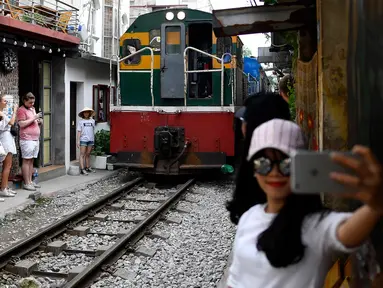 Foto pada 8 Juni 2019 menunjukkan seorang wanita berswafoto saat sebuah kereta melintasi jalur kereta api populer di Hanoi. Di ibu kota Vietnam tersebut rel-rel kereta yang berada di permukiman padat penduduk dijadikan destinasi wisata selfie. (Photo by Manan VATSYAYANA / AFP)