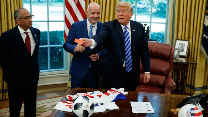 Presiden AS, Donald Trump menyodorkan kartu merah yang diberikan presiden FIFA, Gianni Infantino ke arah jurnalis yang meliput pertemuan mereka di Oval Office Gedung Putih pada Selasa (28/8). (AP/Evan Vucci)