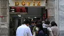 Orang-orang menunggu di luar agen penukaran mata uang dekat alun-alun Taksim ketika lira Turki terperosok ke level terendah sepanjang sejarah di Istanbul, Senin (25/10/2021). Lira melemah imbas pengusiran duta besar AS dan sembilan negara Barat lainnya oleh Presiden Tayyip Erdogan. (Ozan KOSE/AFP)