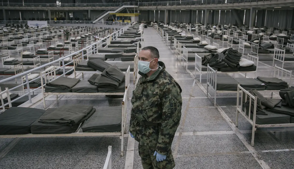 Tentara Serbia berdiri di antara tempat tidur di dalam aula Belgrade Fair yang diubah menjadi rumah sakit sementara virus Corona, Selasa (24/3/2020). Sebanyak 3000 tempat tidur disiapkan untuk  menangani pasien dengan gejala ringan corona Covid-19. (Vladimir Zivojinovic/AFP)