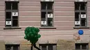 Seorang pria membawa balon melewati lembaran dengan huruf Z, yang telah menjadi simbol militer Rusia, dipajang di jendela selama perayaan menandai peringatan 318 tahun kota Kronstadt, di luar St. Petersburg, Rusia (21/5/2022). (AP Photo/Dmitri Lovetsky)