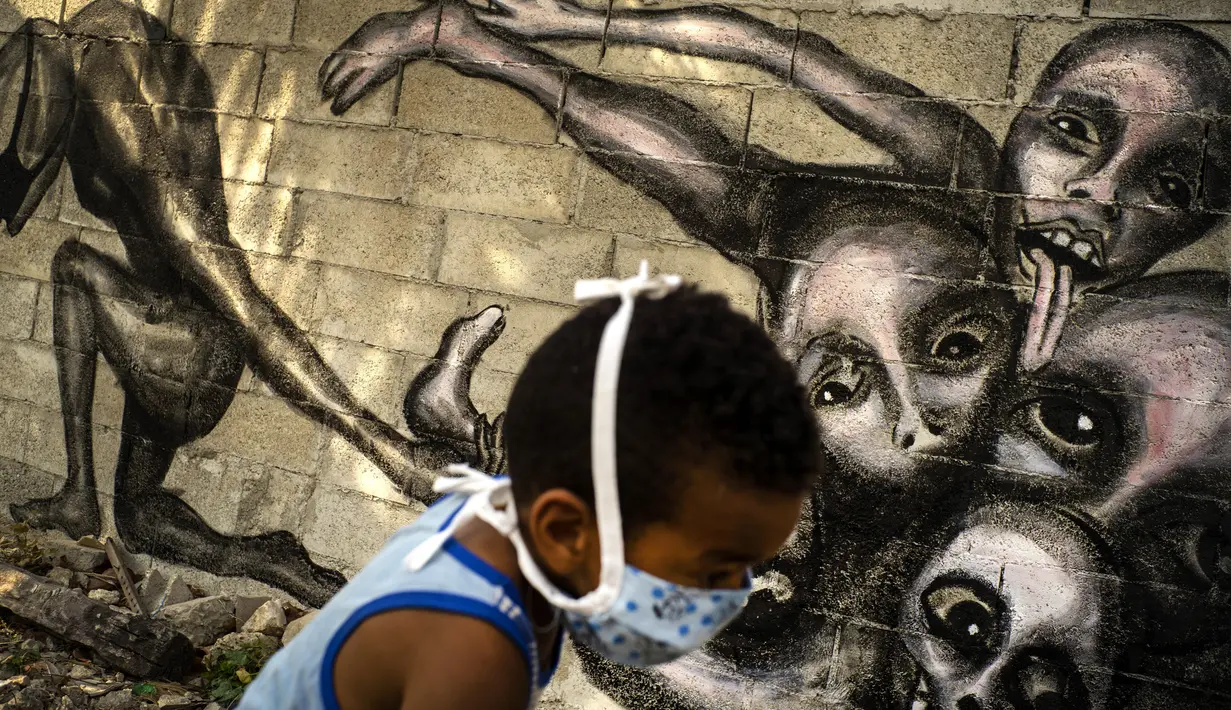 Seorang anak yang mengenakan masker lewat di depan mural berjudul ‘Marcha Hacia la Oscuridad’ atau ‘Move Toward Darkness’ karya seniman Yulier P. di Havana, Kuba, Jumat (10/4/2020). Yulier P. mengatakan muralnya menunjukkan ketidakberdayaan manusia menghadapi COVID-19. (AP Photo/Ramon Espinosa)