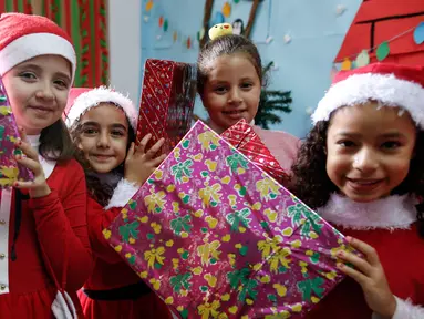 Sejumlah anak Palestina mengenakan kostum santa claus sambil membawa kado berpose saat perayaan menyambut Hari Natal di Sekolah Amerika di Kota Gaza (20/12).  (AFP Photo/Mohammed Abed)