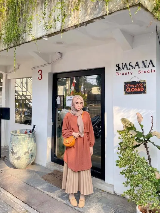 Busana tunic bisa jadi opsi OOTD saat cuaca dingin, padukan dengan rok plisket dan hijab warna nude serta mini sling bag. (Instagram/richaeu).