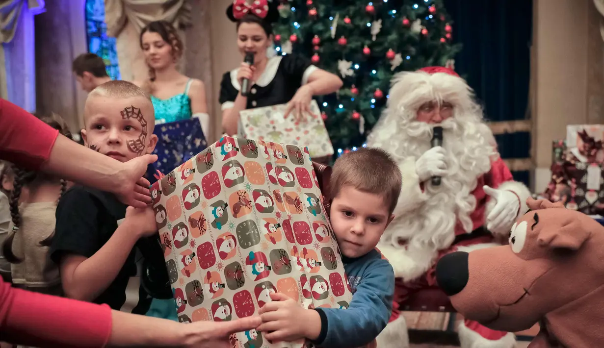 Anak-anak menerima hadiah saat acara Natal untuk anak-anak keluarga militer di Bucharest, Rumania, (21/12). Para ayah anak-anak tersebut sedang bertugas melayani misi pemelihara perdamaian internasional di National Military Circle. (AP Photo/Vadim Ghirda)