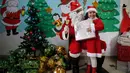 Seorang anak Palestina mengenakan kostum santa claus sambil membawa kado berpose dengan santa claus saat perayaan menyambut Hari Natal di Sekolah Amerika di Kota Gaza (20/12).  (AFP Photo/Mohammed Abed)