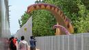 Orang-orang berhenti untuk mengambil foto replika dinosaurus seukuran aslinya yang dipajang di sepanjang "Changi Jurassic Mile" jalan santai di Singapura (13/10/2020). Singapura membangun replika-replika dinosaurus di jalur menunju bandara Changi. (AFP/Roslan Rahman)