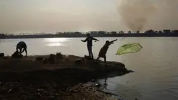 Orang-orang memancing di dasar sungai Paraguay yang terbuka, saat kolom asap membubung di pantai lain, di tengah kekeringan bersejarah yang mempengaruhi ketinggian sungai, di Mariano Roque Alonso, Paraguay, Senin (20/9/2021).  (AP Photo/Jorge Saenz)