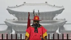 Seorang 'penjaga istana' berdiri untuk turis di depan Istana Gyeongbokgung yang tertutup salju di pusat kota Seoul (19/1/2022). Pihak berwenang di Seoul dan daerah sekitarnya pada Rabu (19/1) tetap waspada karena wilayah ibu kota diperkirakan akan turun salju lebat sepanjang hari. (AFP/Jung Yeon-je)