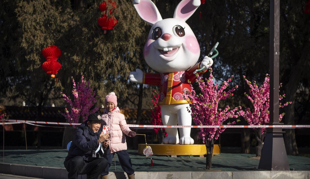 Seorang pria dan wanita berpose untuk selfie di depan patung kelinci untuk Tahun Baru Imlek mendatang di sebuah taman umum di Beijing, Jumat, 20 Januari 2023. Berbagai hiasan dan pernak-pernik mulai menghiasi Taman di Beijing menjelang perayaan Tahun Baru Imlek. (AP Photo/Mark Schiefelbein)