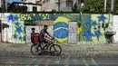 Pengendara sepeda melintasi mural Piala Dunia 2018 bergambar bendera Brasil di jalanan Camboata, Rio de Janeiro, Brasil, Kamis (31/6). (Fabio TEIXEIRA/AFP)