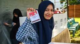 Hari ini, Rabu 27 November 2024, masyarakat Indonesia menggunakan hak politiknya untuk memilih pemimpin daerah dalam Pilkada Serentak 2024. Tampak dalam foto, seorang perempuan menunjukkan kertas suara saat pemilihan kepala daerah di Darul Imarah, pinggiran Banda Aceh, pada 27 November 2024. (CHAIDEER MAHYUDDIN/AFP)